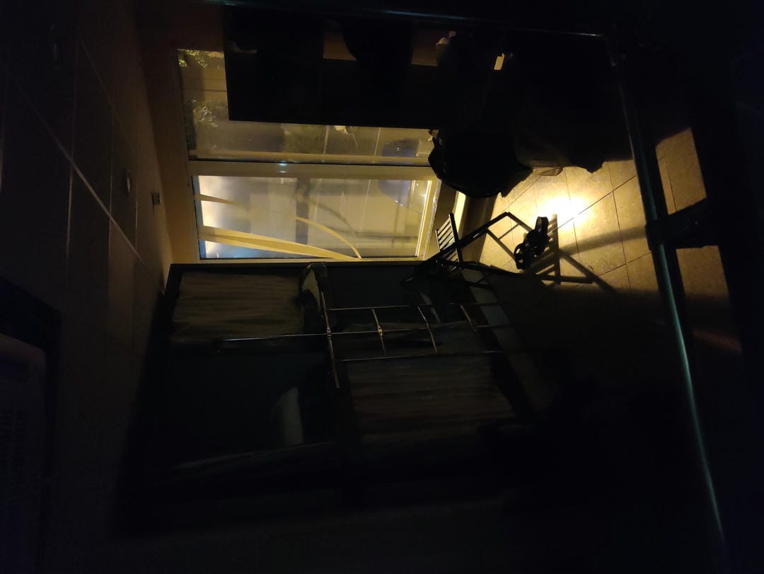 Dim room with faint window light, containing beds and miscellaneous items.