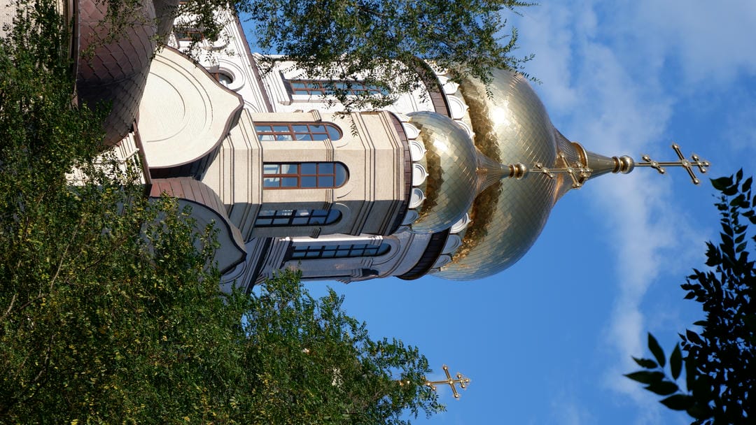 Golden church dome and cross standing out against blue sky.