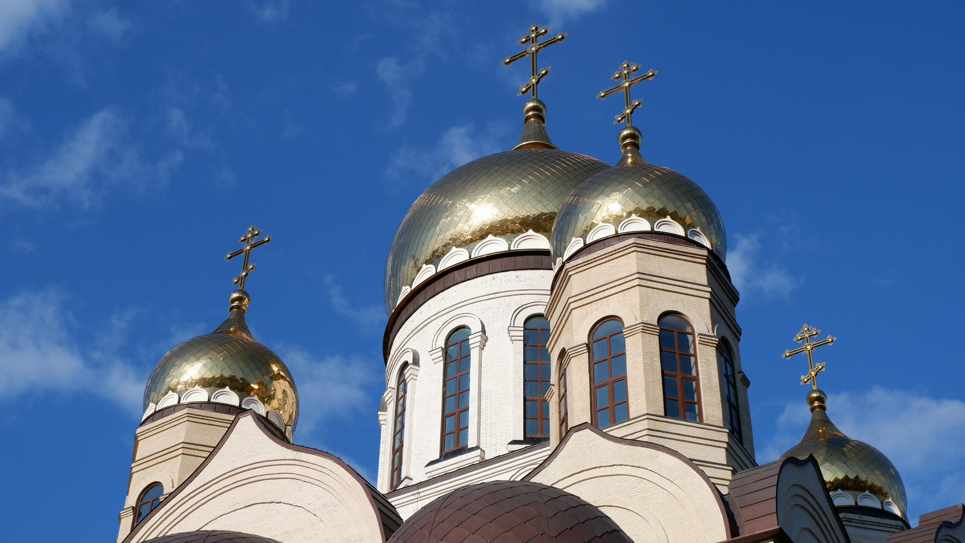 Three church towers with golden domes and crosses under clear sky.