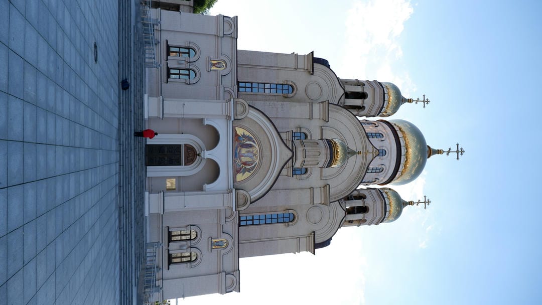 Large church with multiple golden domes, person standing on front steps.