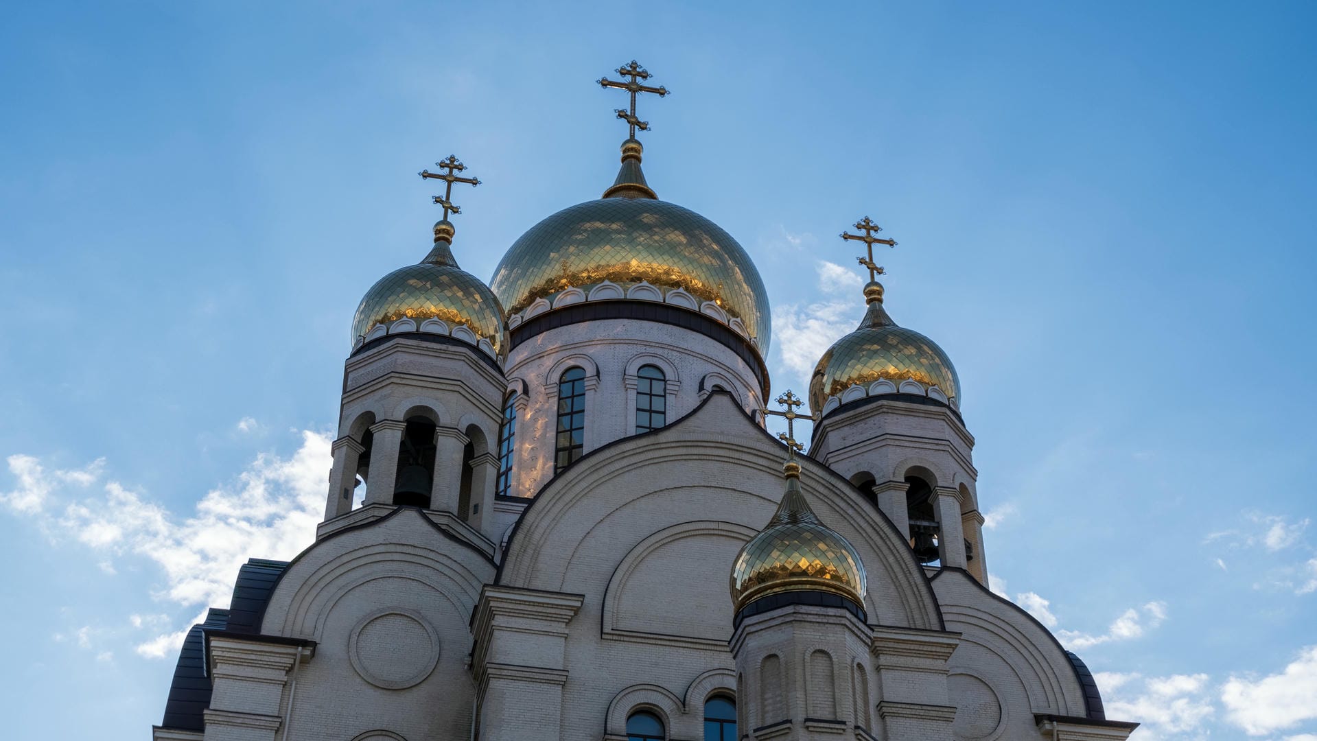 Three golden-domed church towers under blue sky with clouds.