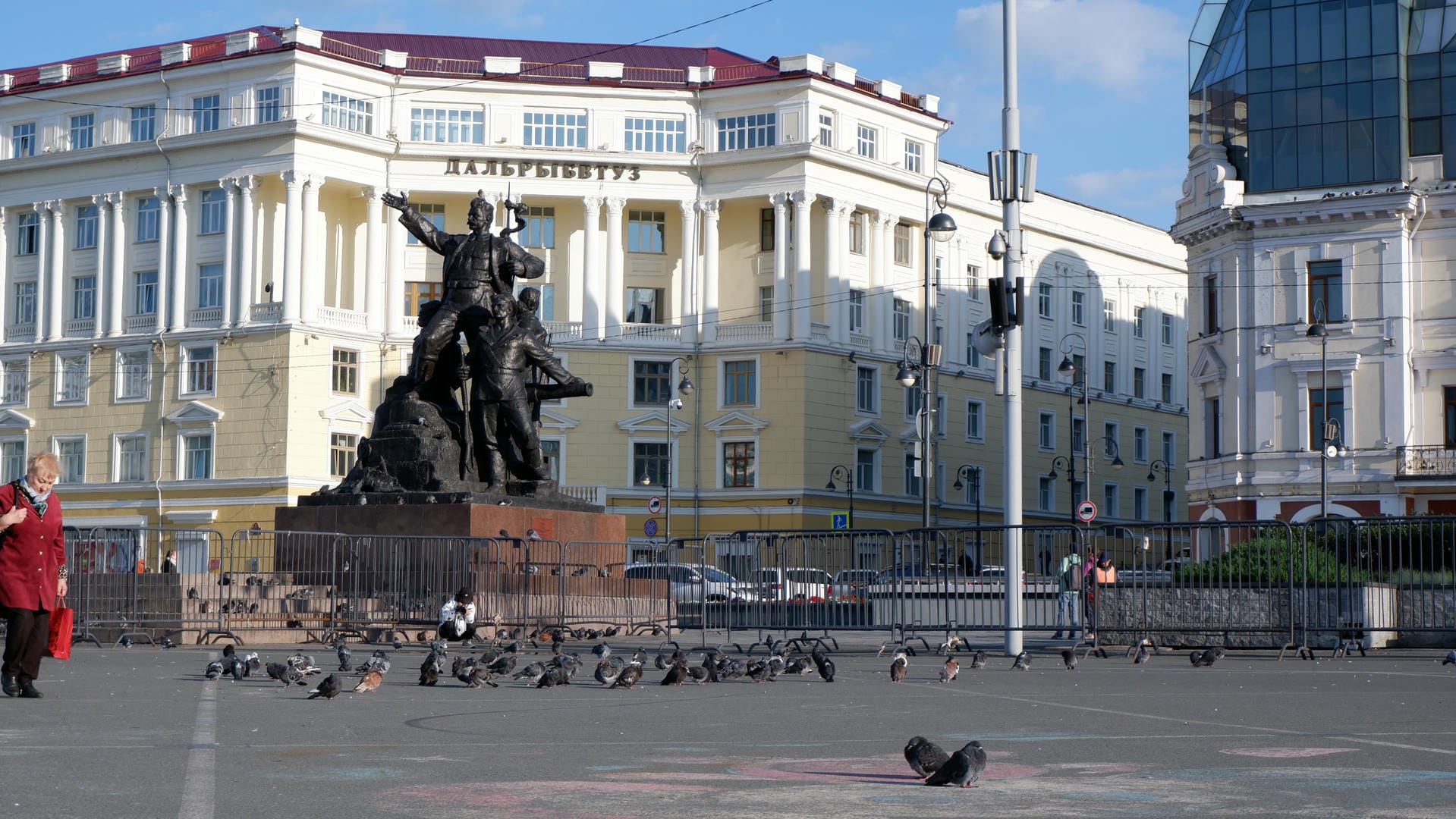 Square filled with pigeons, large building and statue in background.