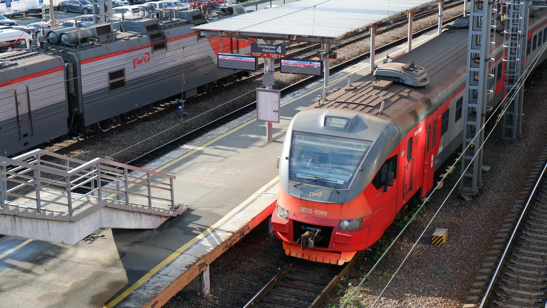 Red train parked at platform next to gray railway car.
