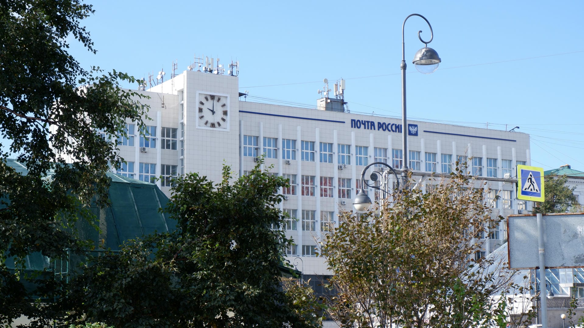 Building partially obscured by trees, “Почта России” sign visible, glass dome structure on right.
