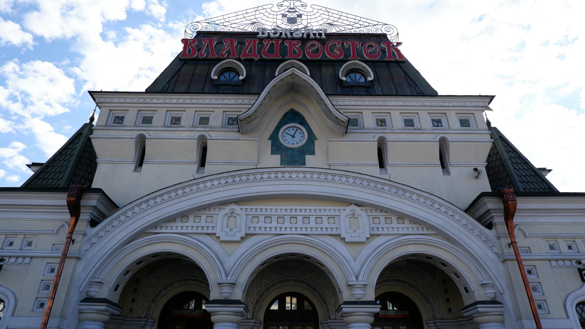 White building with red Cyrillic “Владивосток” sign and central clock decoration.