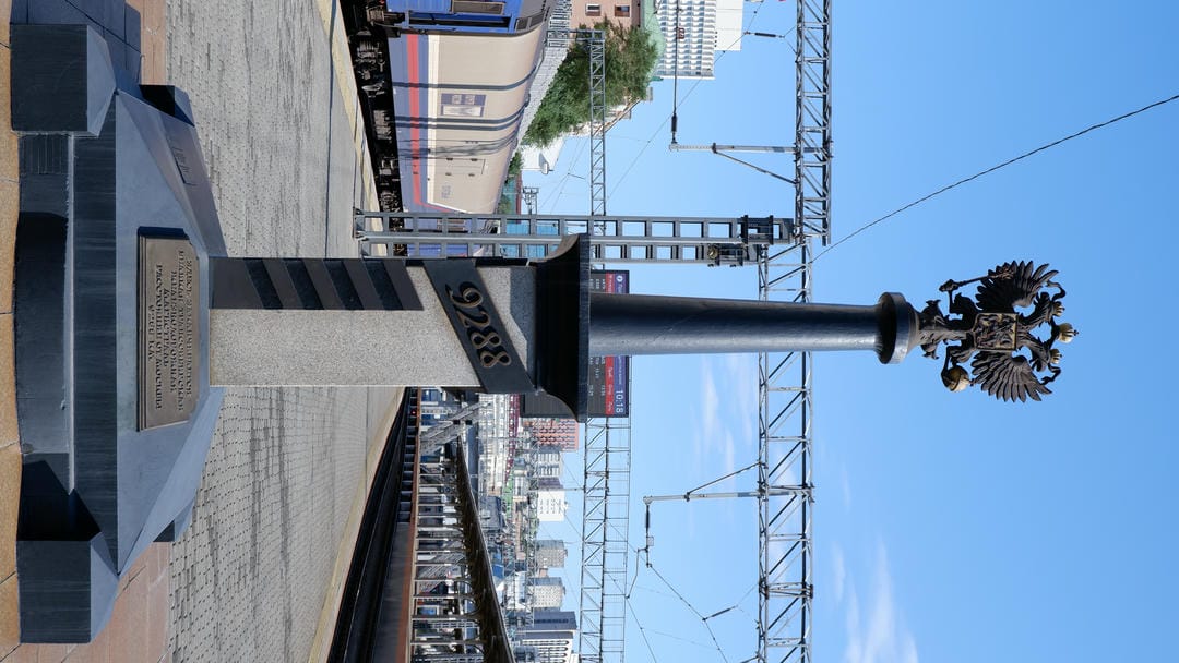 Double-headed eagle sculpture on stone pillar marked “9288”, train platform in background.