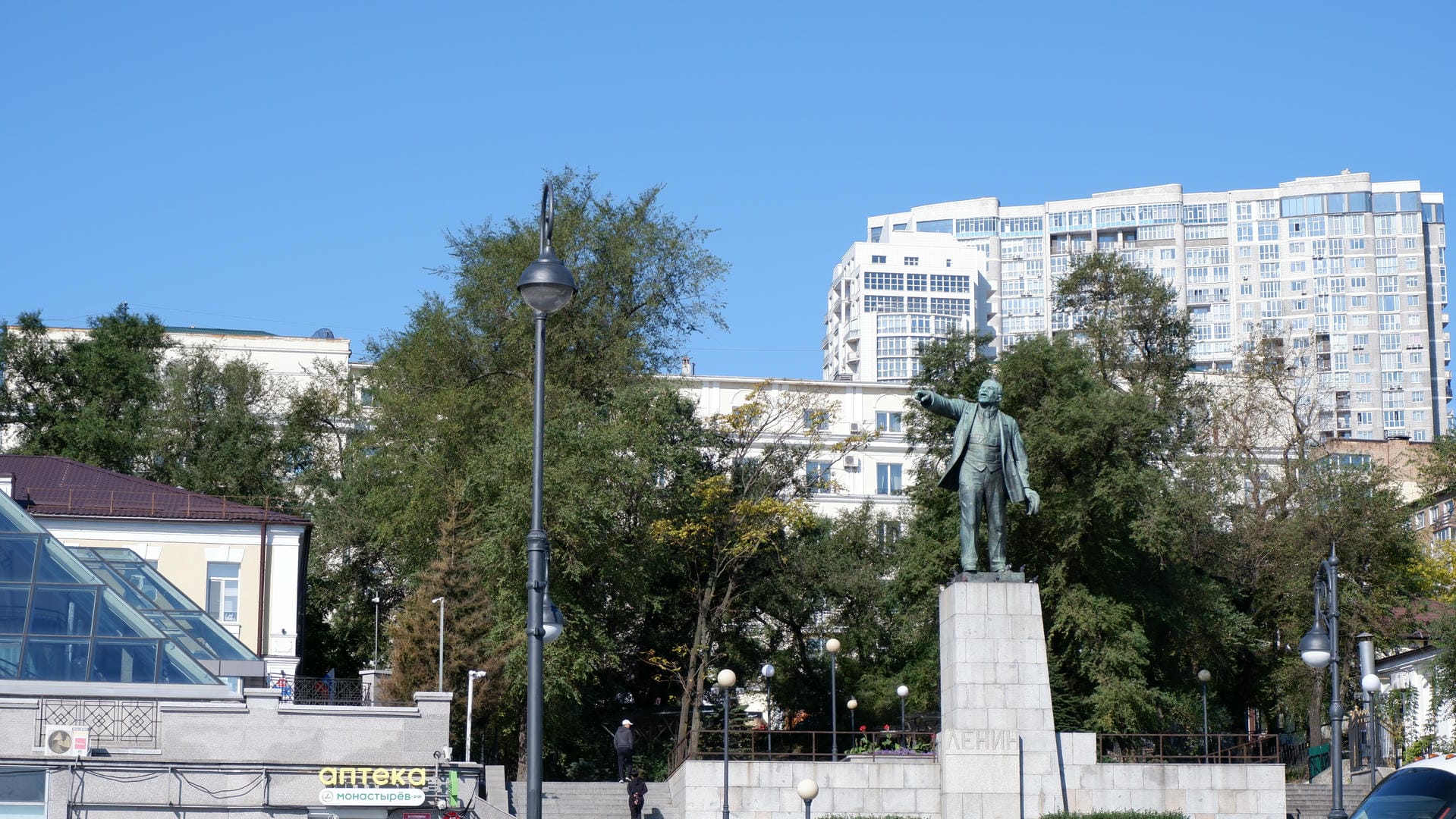 Lenin statue in square with skyscrapers and trees in background.