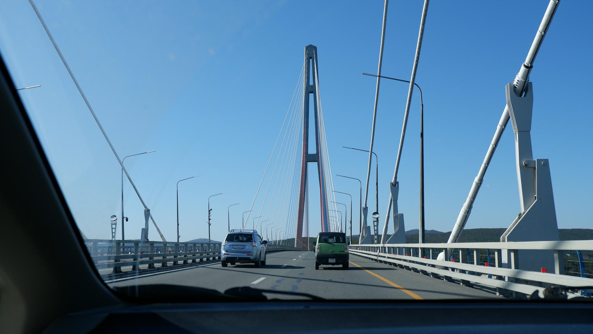 Car window view of bridge with moving traffic under clear sky.