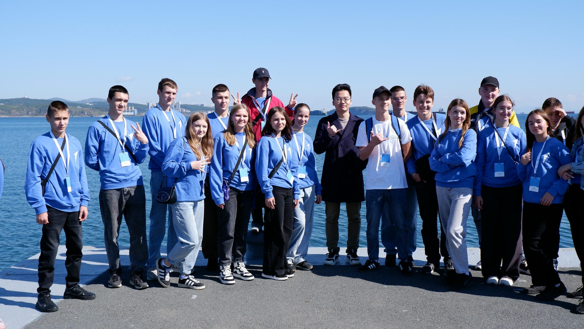 Group in blue clothing posing for group photo with sea and buildings behind.