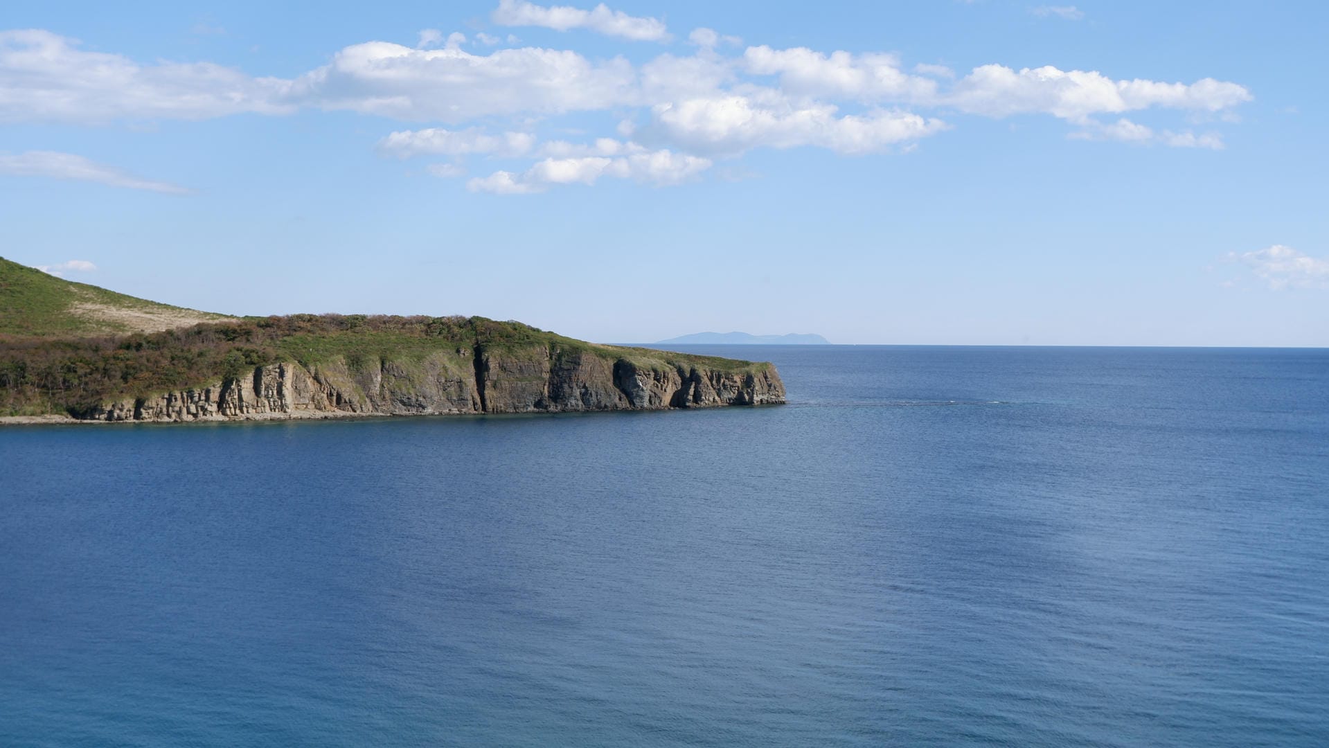 Blue sea and cliffs under partly cloudy sky.