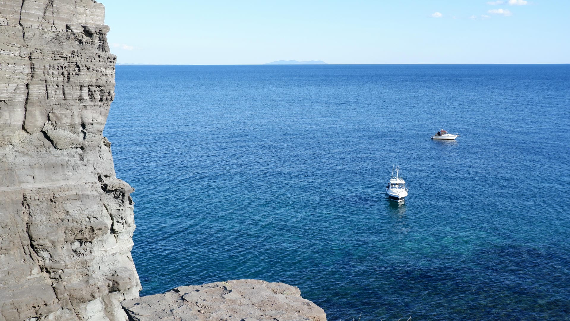 Two boats anchored in deep blue sea near rocky coast.