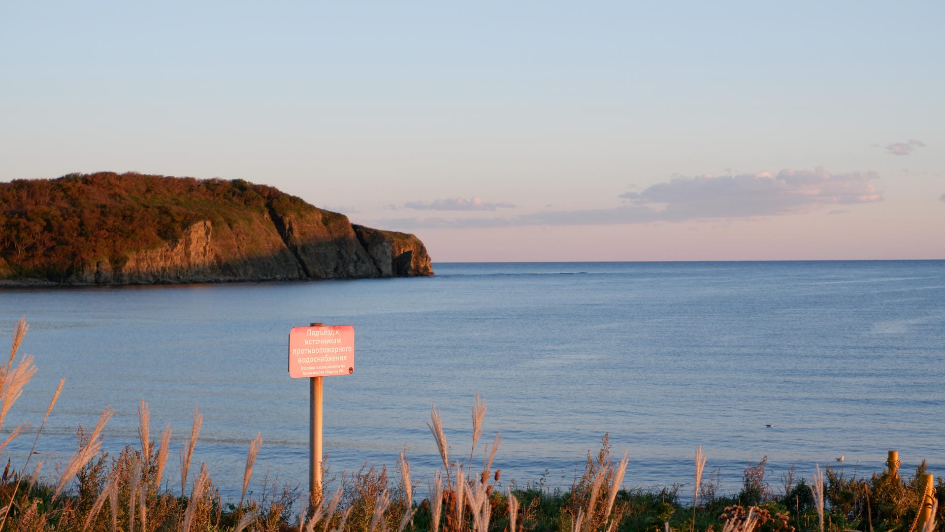 Orange sign with Cyrillic text at seaside cliff.
