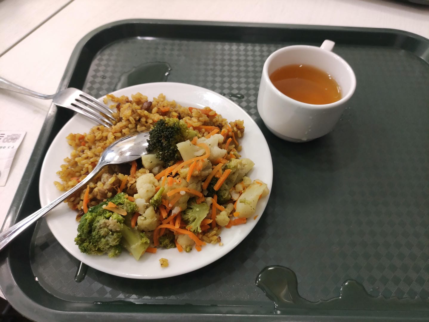Tray holding fried rice, vegetables, tea, and utensils.