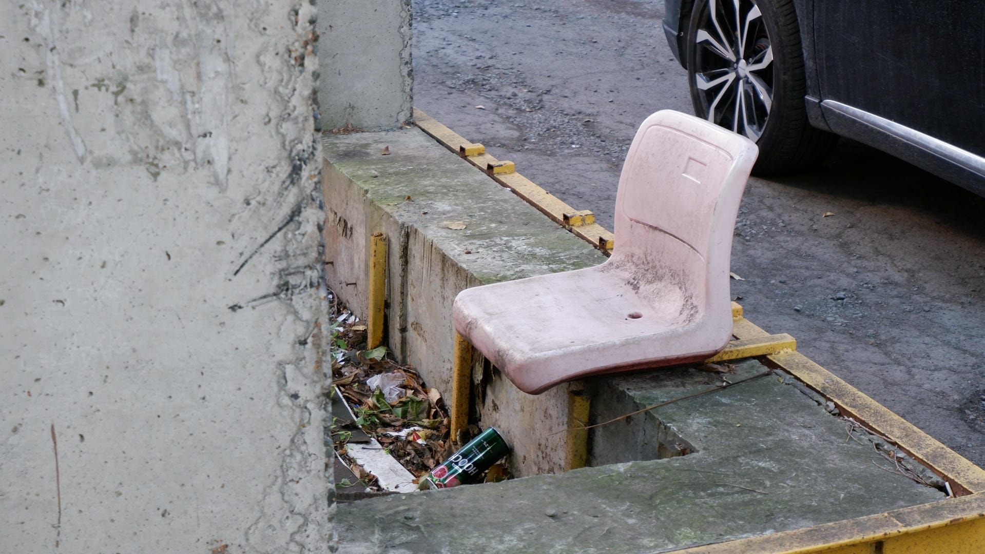 A pink plastic chair placed by the roadside with scattered trash nearby.