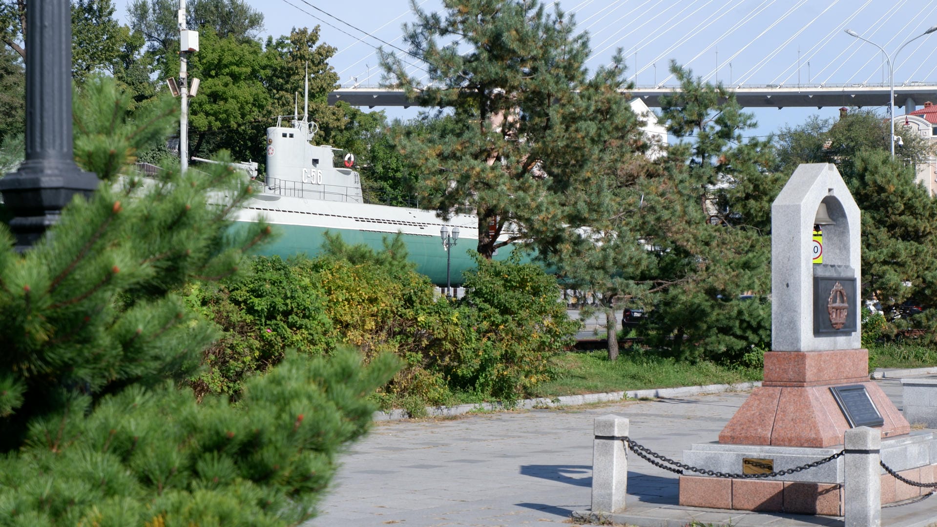A green submarine displayed in a park, surrounded by trees and monuments.