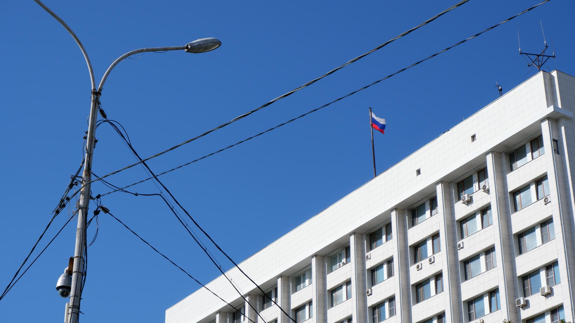 The Russian flag flying atop a building with utility poles and lampposts in front.