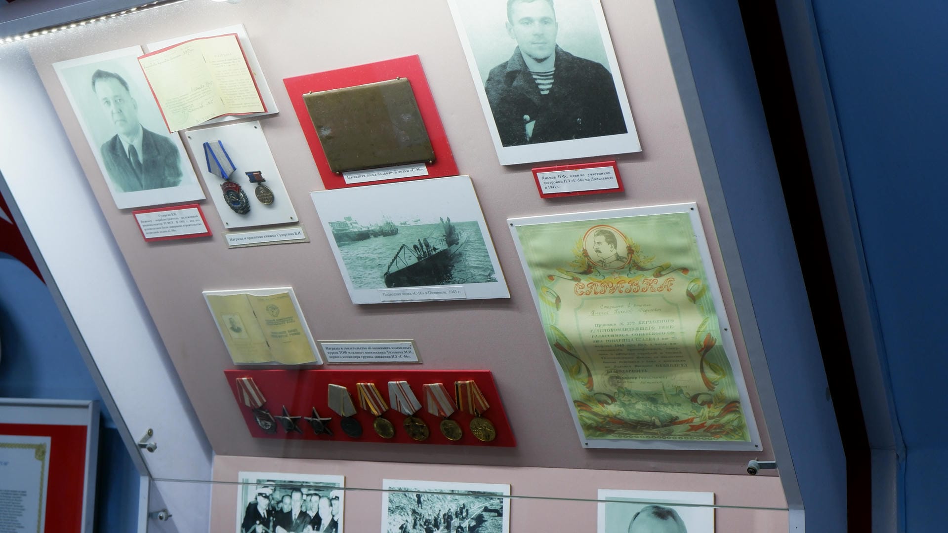 A display case in a museum showing historical artifacts, photographs, medals, and certificates.