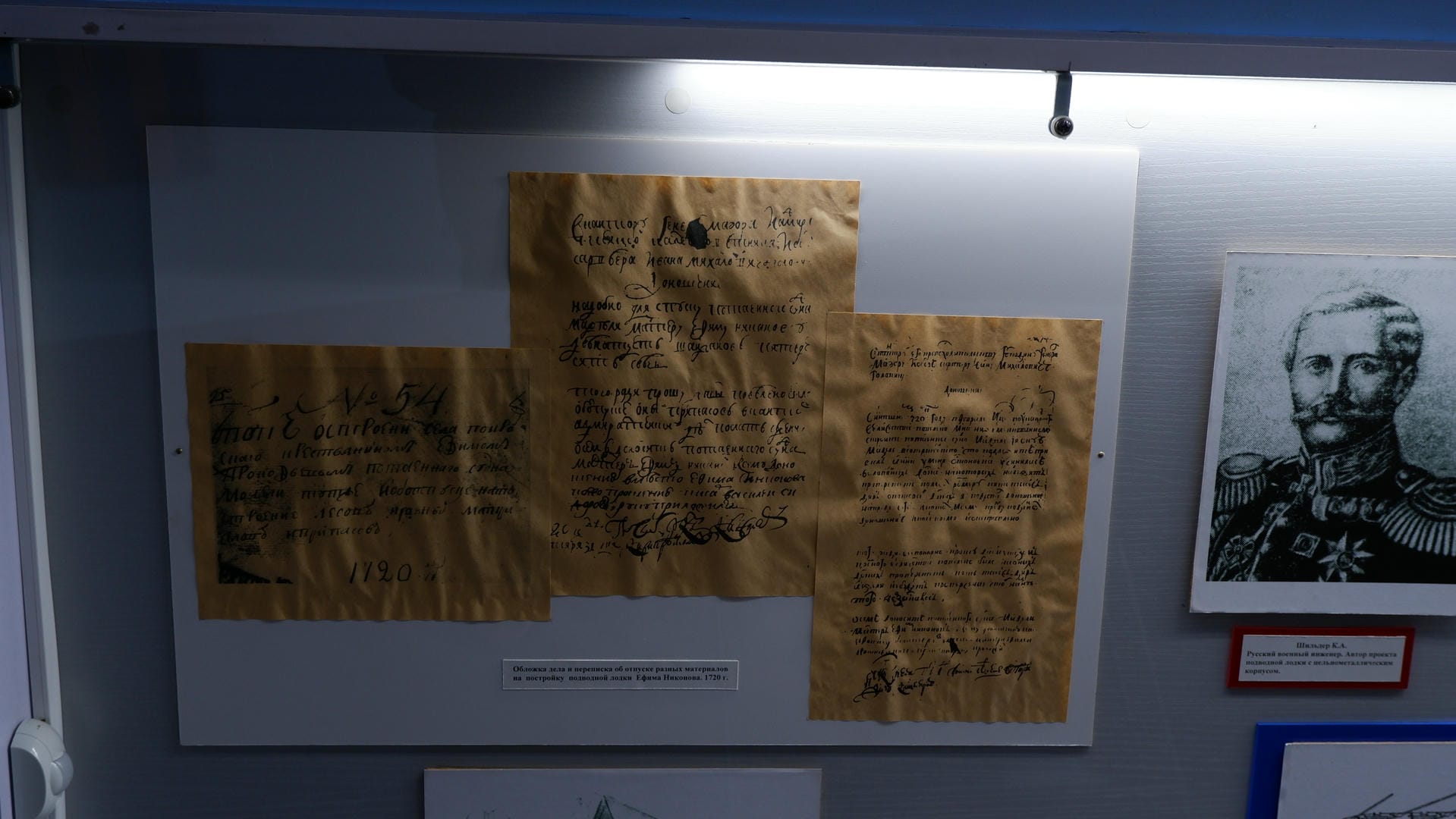 Three old documents and a photograph of a soldier hanging on the wall.