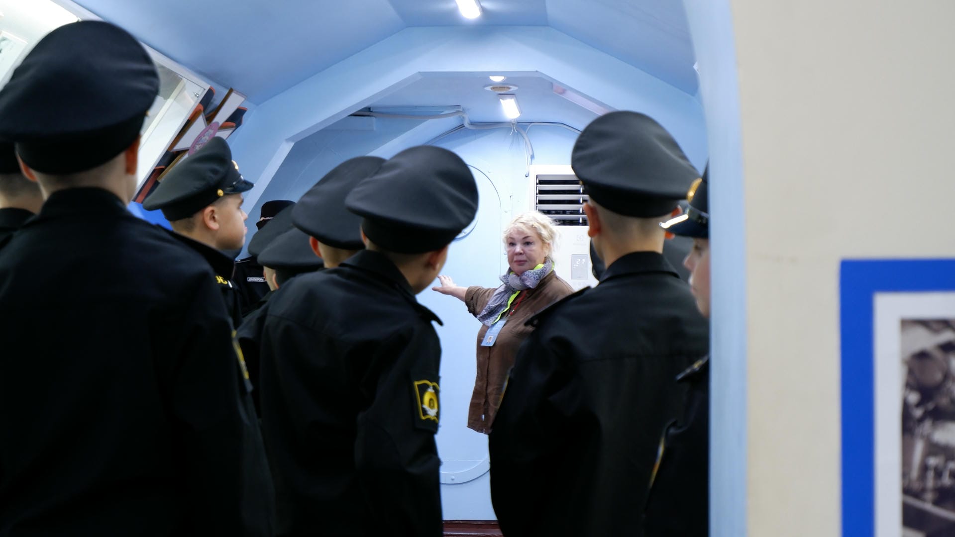 A group of students in uniform listening to a woman giving a lecture.