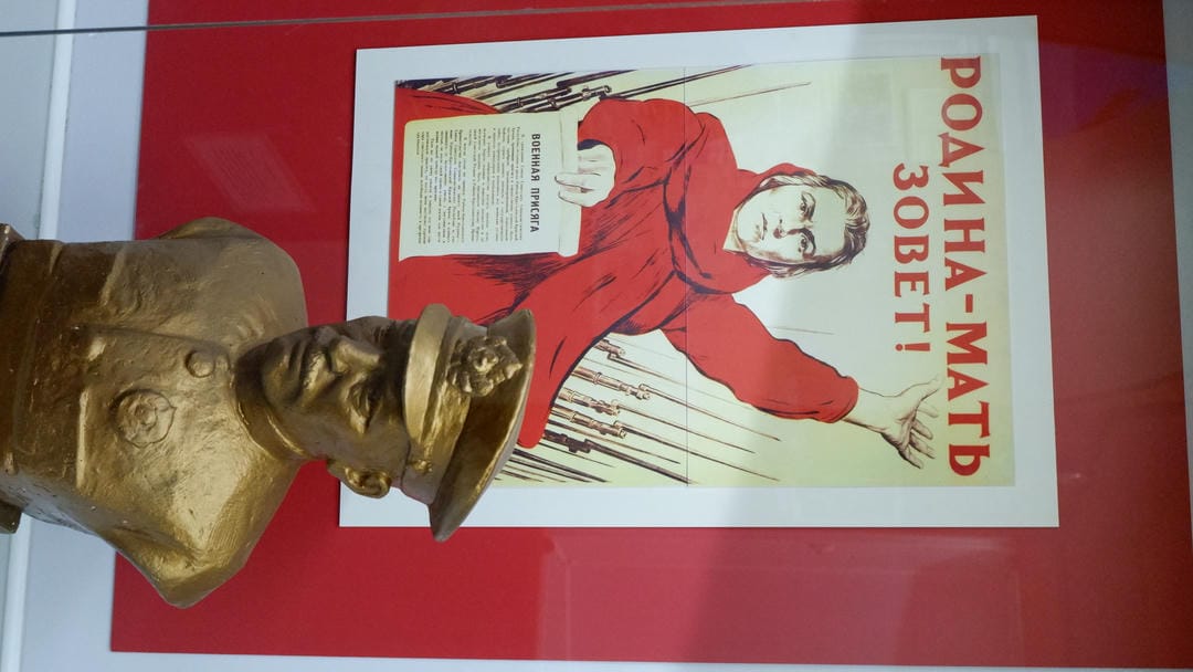 A poster reads “Motherland is calling!” featuring a female figure, with a golden statue in front.