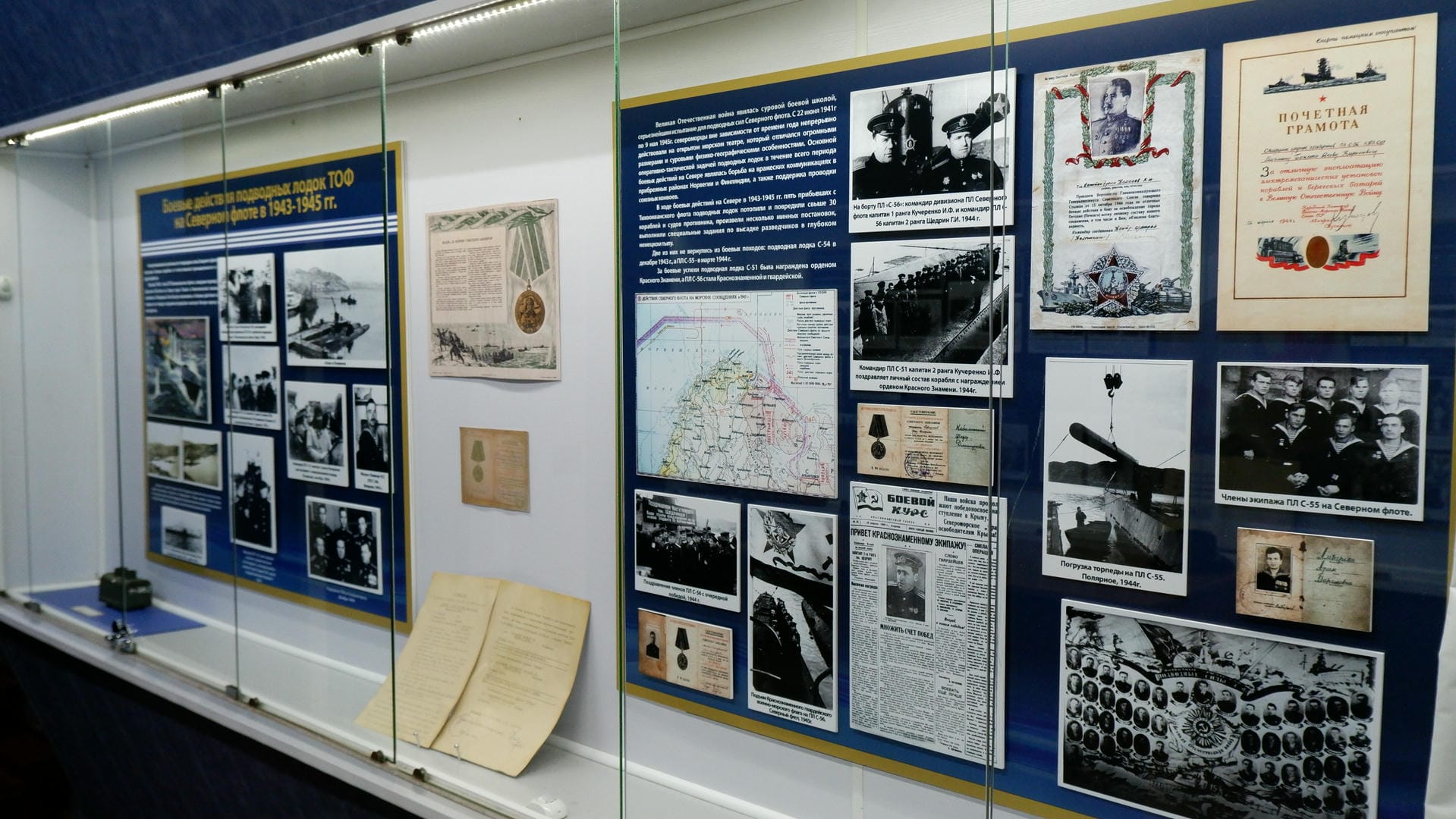 The display case contains military photos, maps, and other historical artifacts from World War II.
