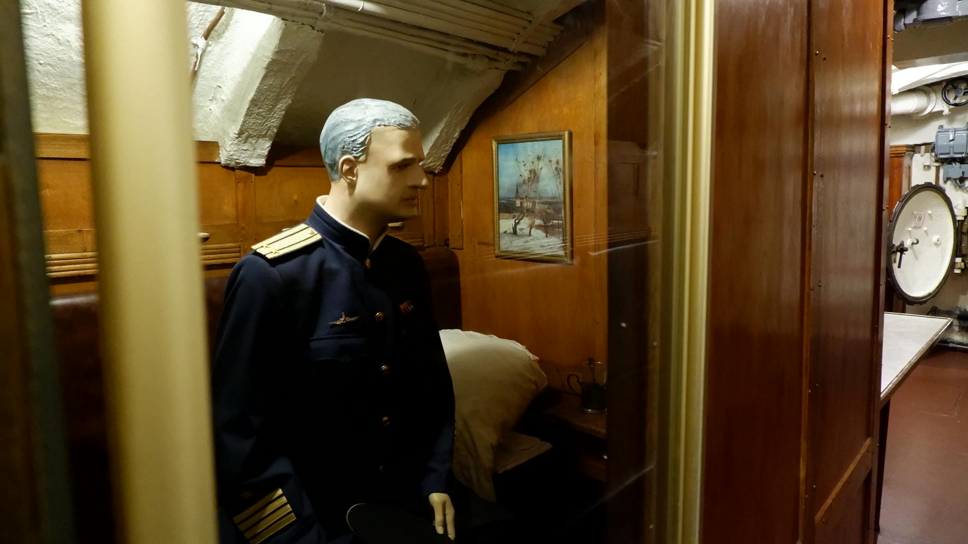 A mannequin dressed in naval uniform stands in the room, next to a bed and a painting.