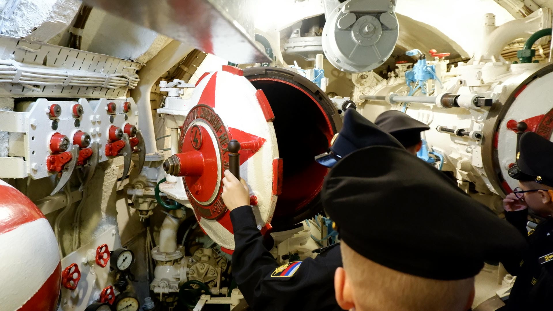 A person operates a red valve inside the submarine, with others watching around.