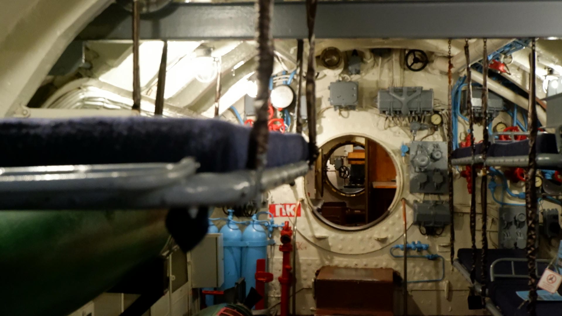 A circular hatch inside the submarine, with a blue object in the foreground and various equipment in the background.