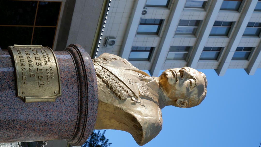 The submarine is docked by the shore, with tall buildings visible in the distance.