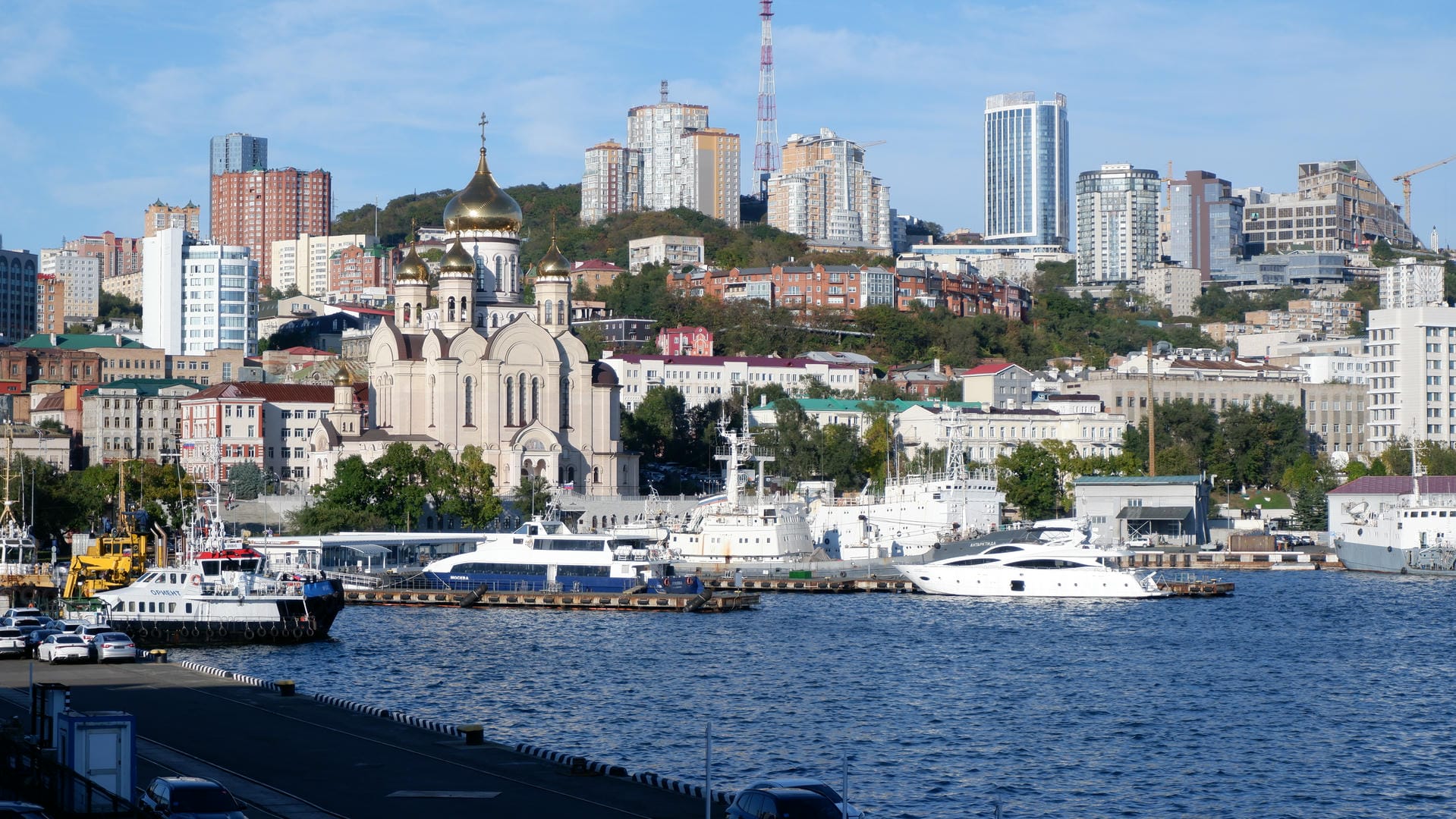 Several boats float on the sea, with the city skyline in the background, including skyscrapers and cranes.