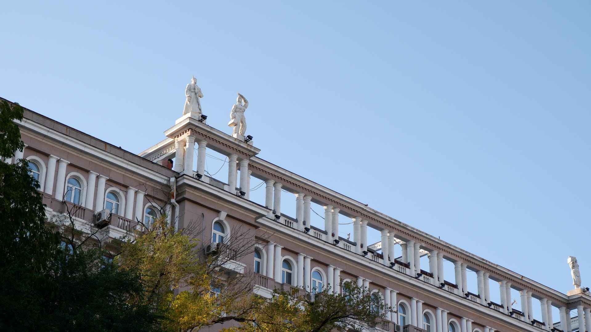 The top of a building is decorated with two white statues, in a classical architectural style.
