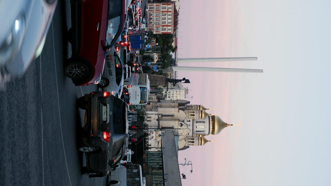 A church with a golden dome, with many vehicles on the road ahead, and the sky glowing with dusk colors.