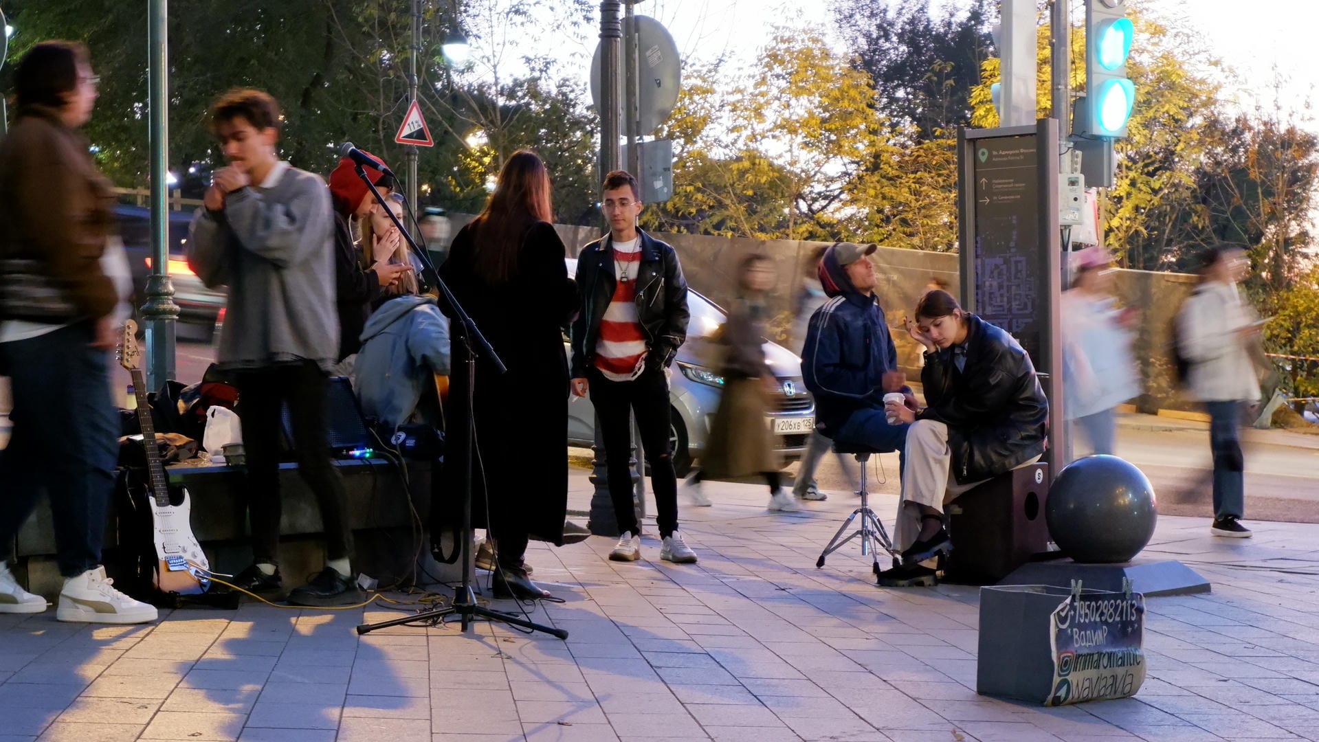 A group of young people performs music on the street, with people stopping to watch.