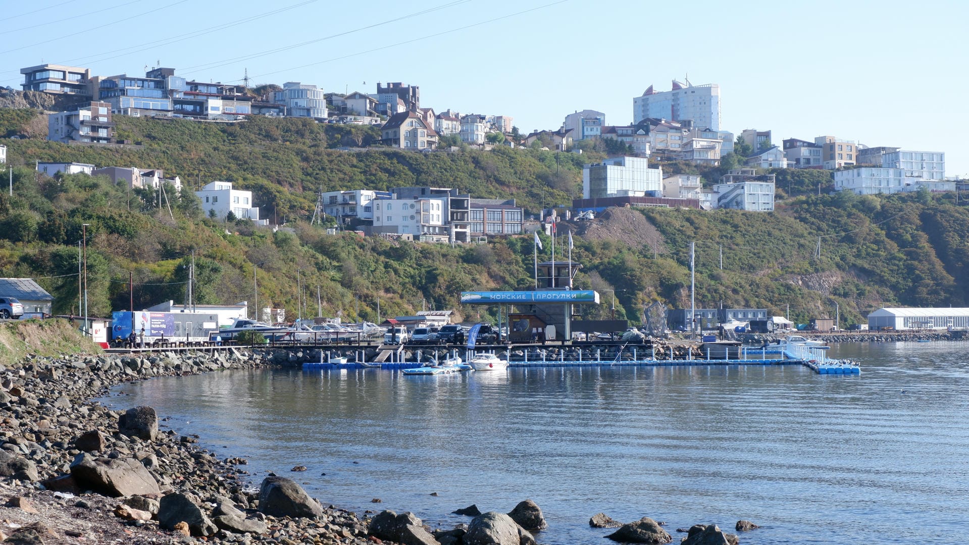 Buildings are scattered on the hillside by the sea, with a dock below where several boats are moored.