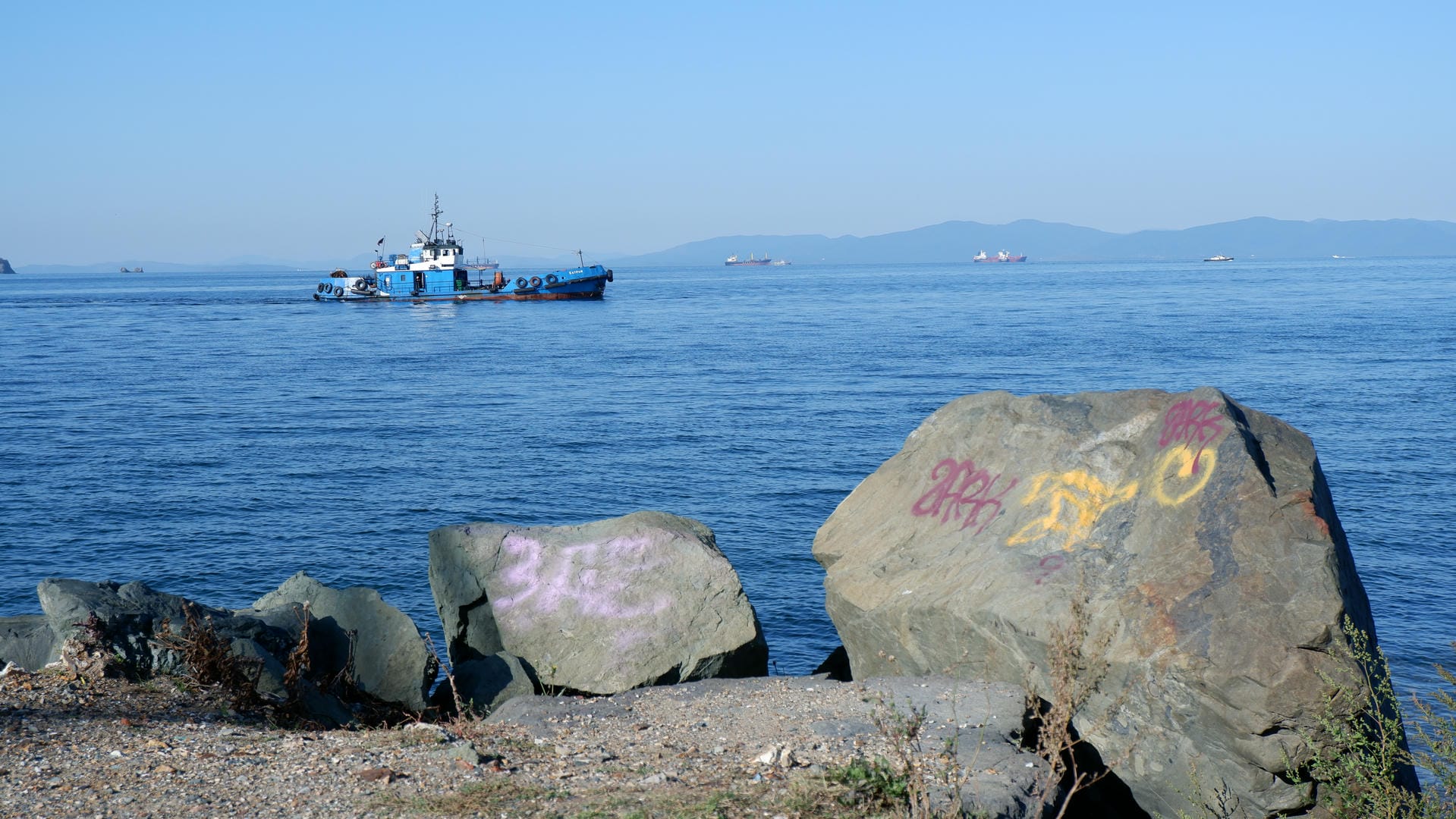 Large rocks along the coast are painted pink and yellow, with a blue boat in the distance.
