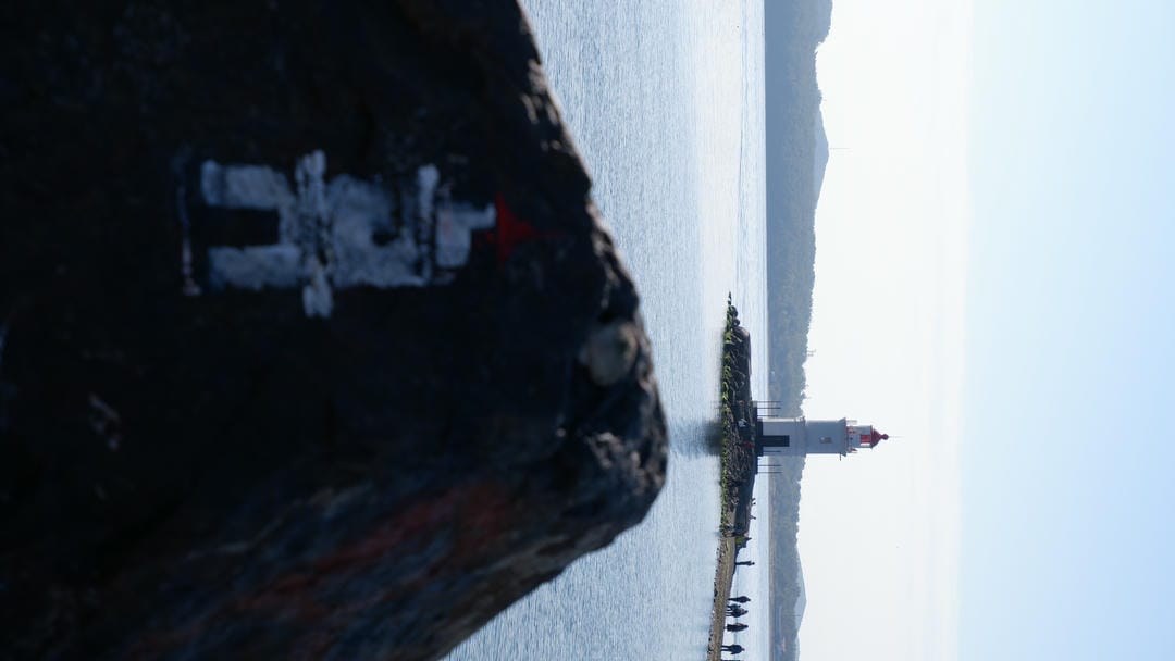 A giant rock is painted with a simple stick figure, with a lighthouse in the background.