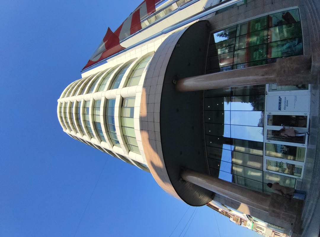 A modern building with a glass facade, two pillars at the entrance, and a person standing nearby.