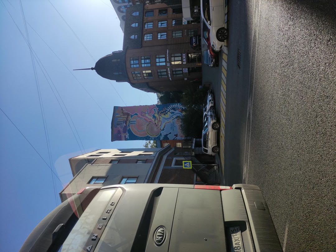 The street has buildings and vehicles, with a gray car on the left and colorful murals in the distance.