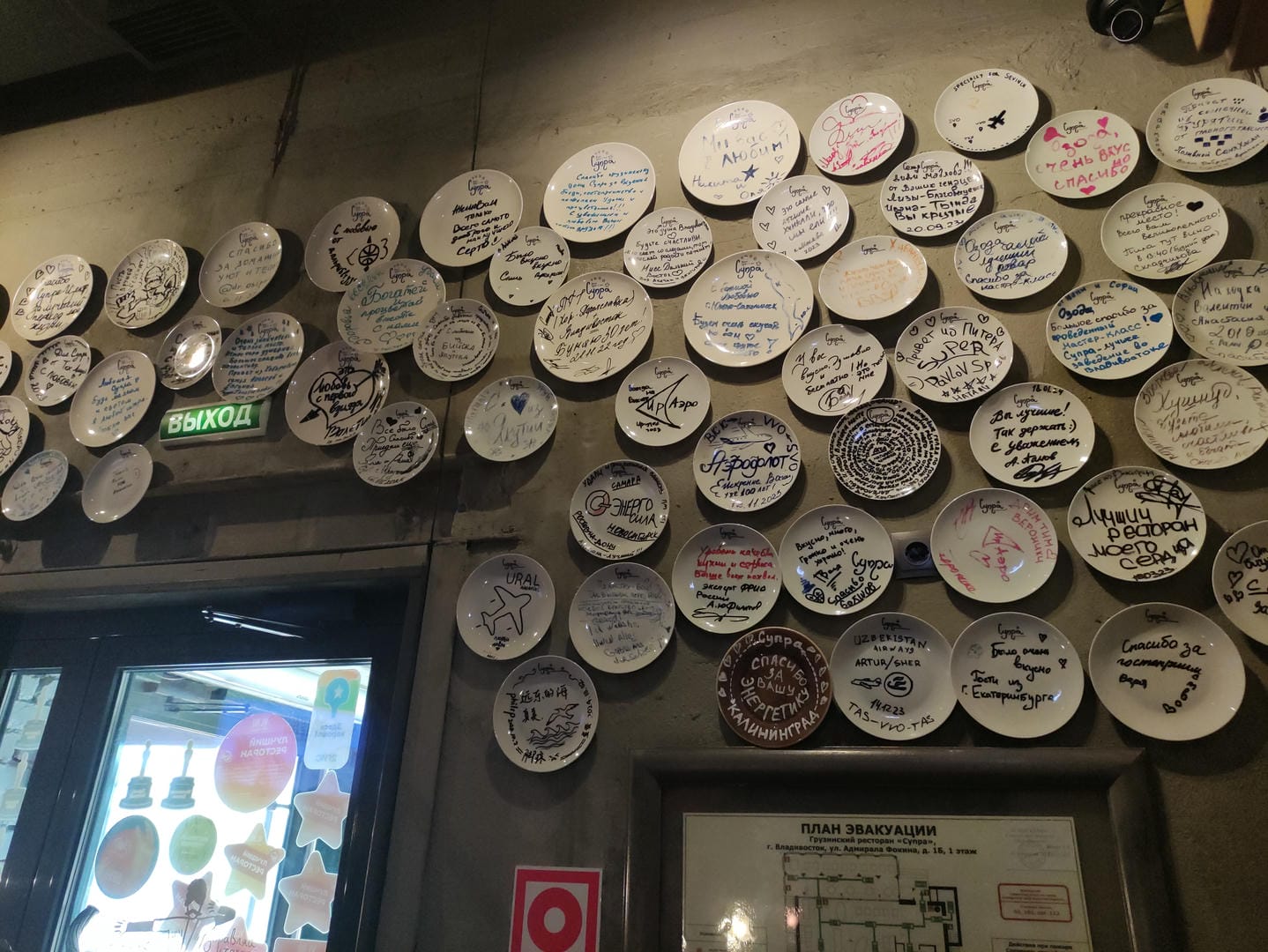 The walls are covered with white plates bearing messages, and there is a green sign above the door.