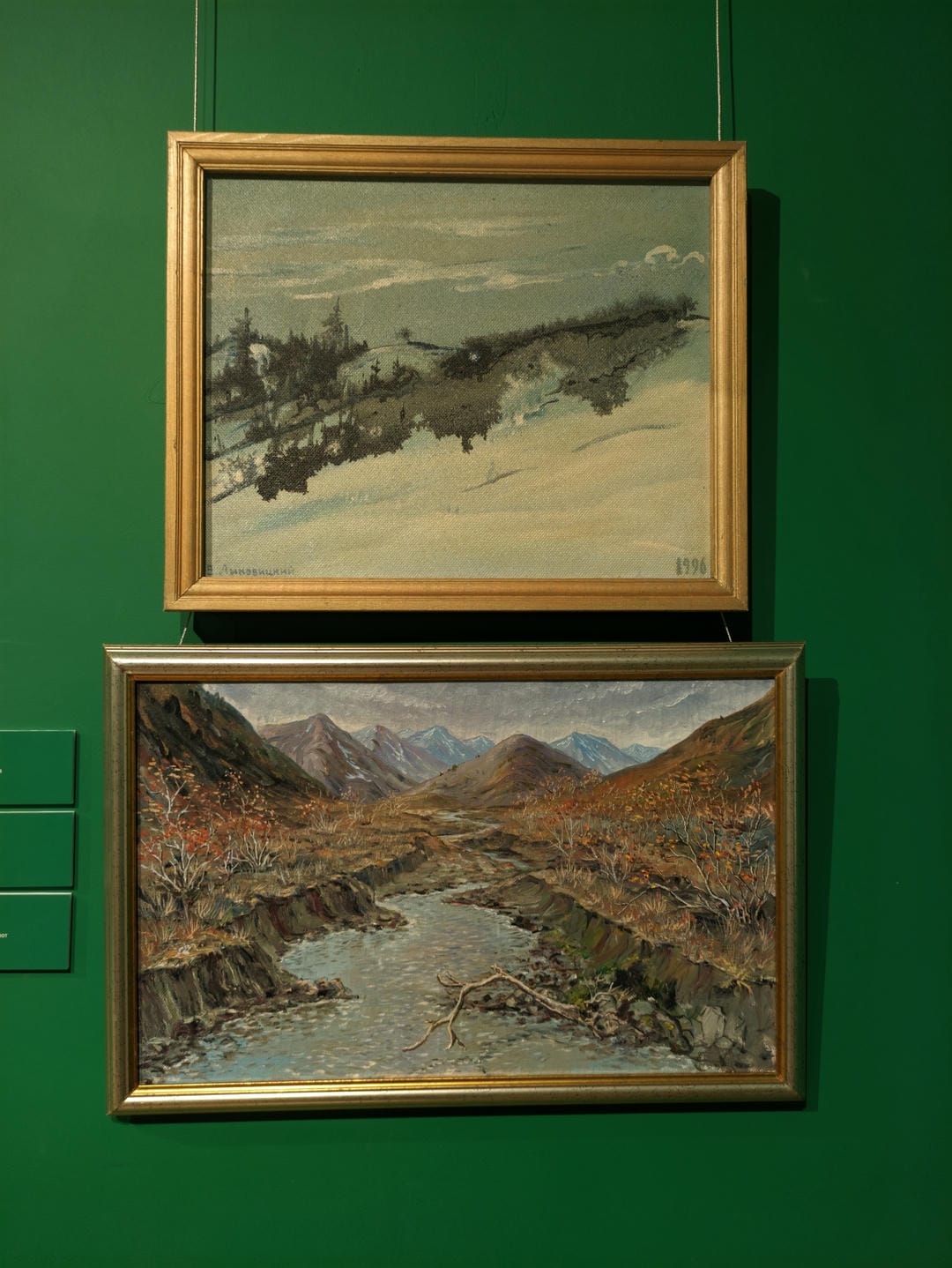 Two paintings hang on a green wall; the upper one depicts snowy trees, while the lower one shows a mountain stream in autumn.