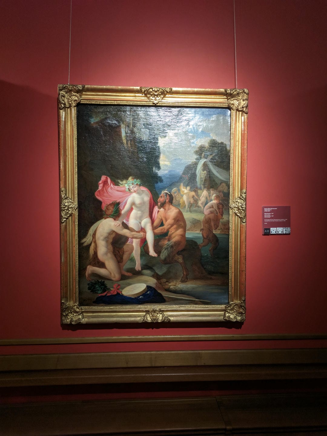 A painting depicts a mythical scene with three nude figures, a woman surrounded by two men, with other figures and animals in the background.