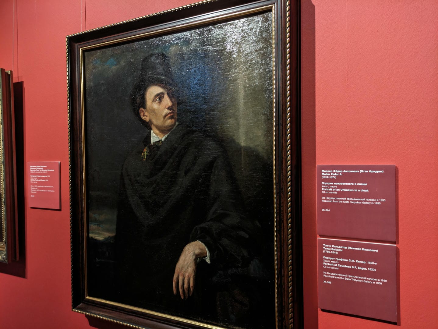 A painting depicts a man in a black cloak and top hat standing sideways, gazing into the distance.