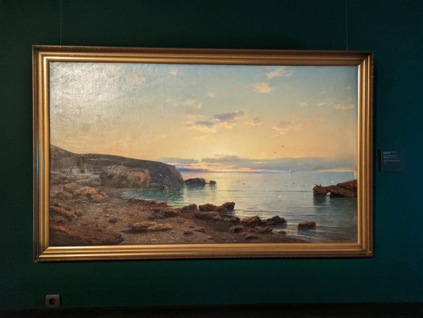A painting depicts a coastal sunset, with rocks, sandy beach, and calm sea.