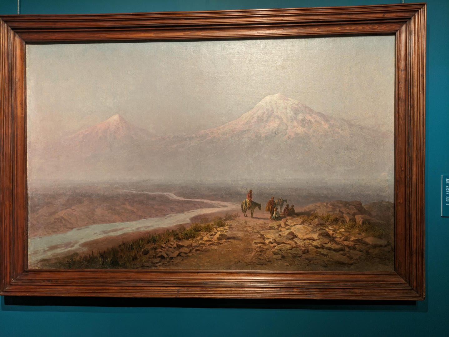 A framed oil painting depicts a mountain scene, with several people and horses in the foreground.