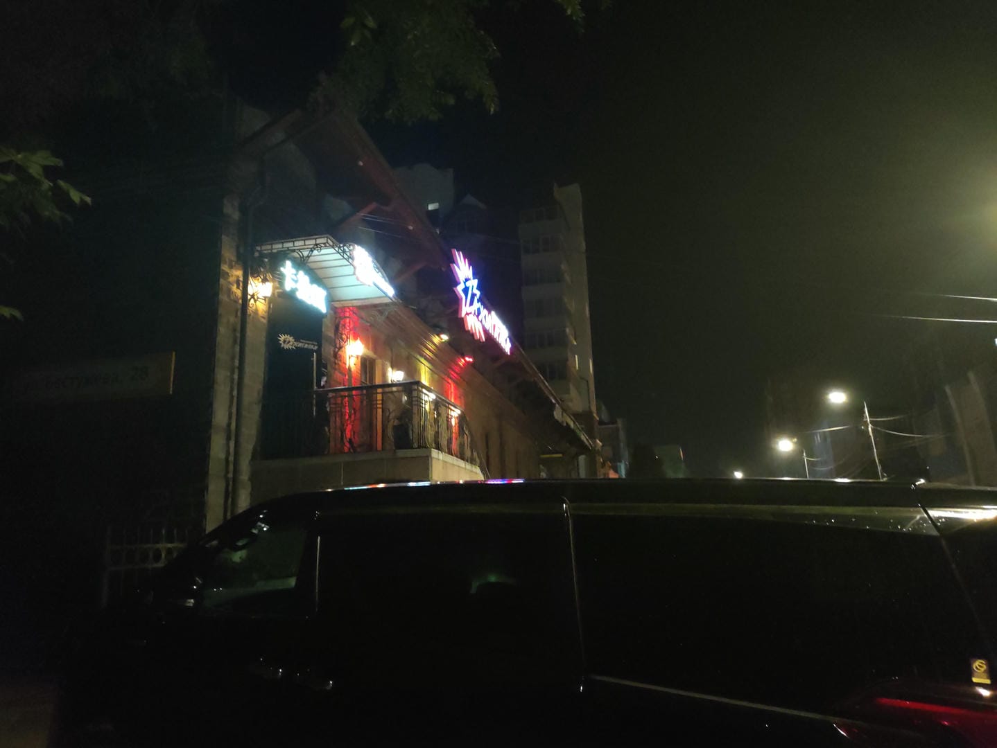 A neon-lit street at night shows buildings and a black car.