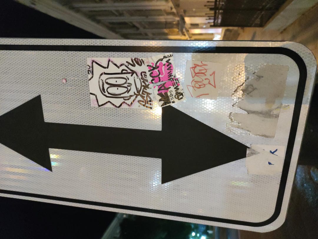 A road sign with arrows indicating directions is covered in graffiti and stickers.