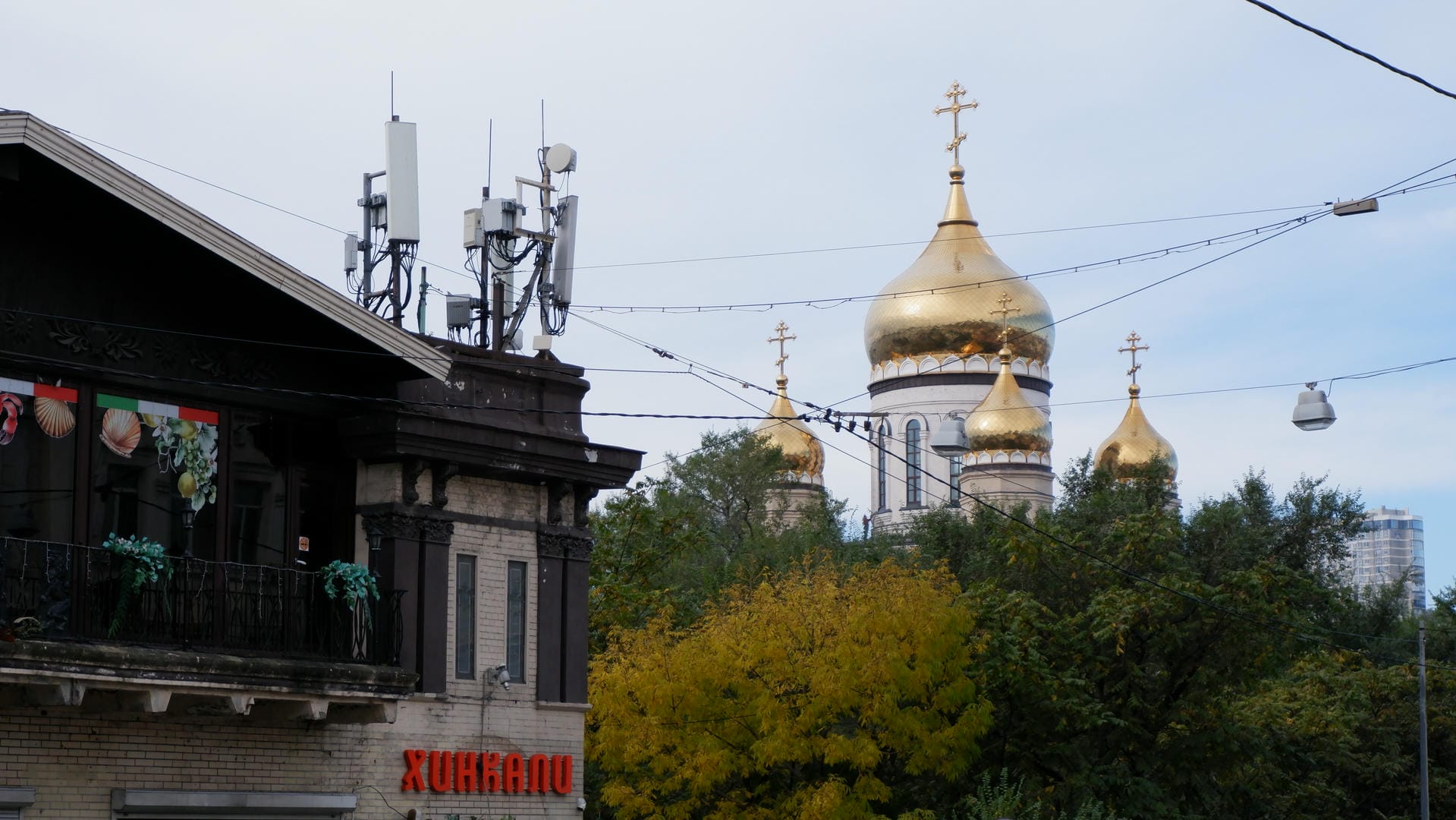 A golden-domed church surrounded by trees and buildings. In the foreground, there is a building with communication equipment installed on top.