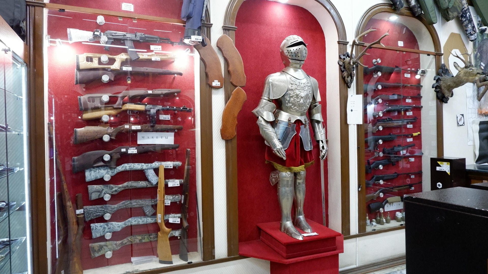 A display cabinet showcasing various firearm accessories, with a red background. In the center stands a knight model wearing armor.