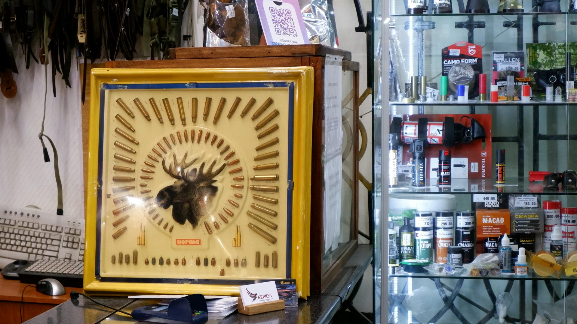 A decorative board displaying bullets arranged in the shape of a deer head, with a hunting supplies store in the background.
