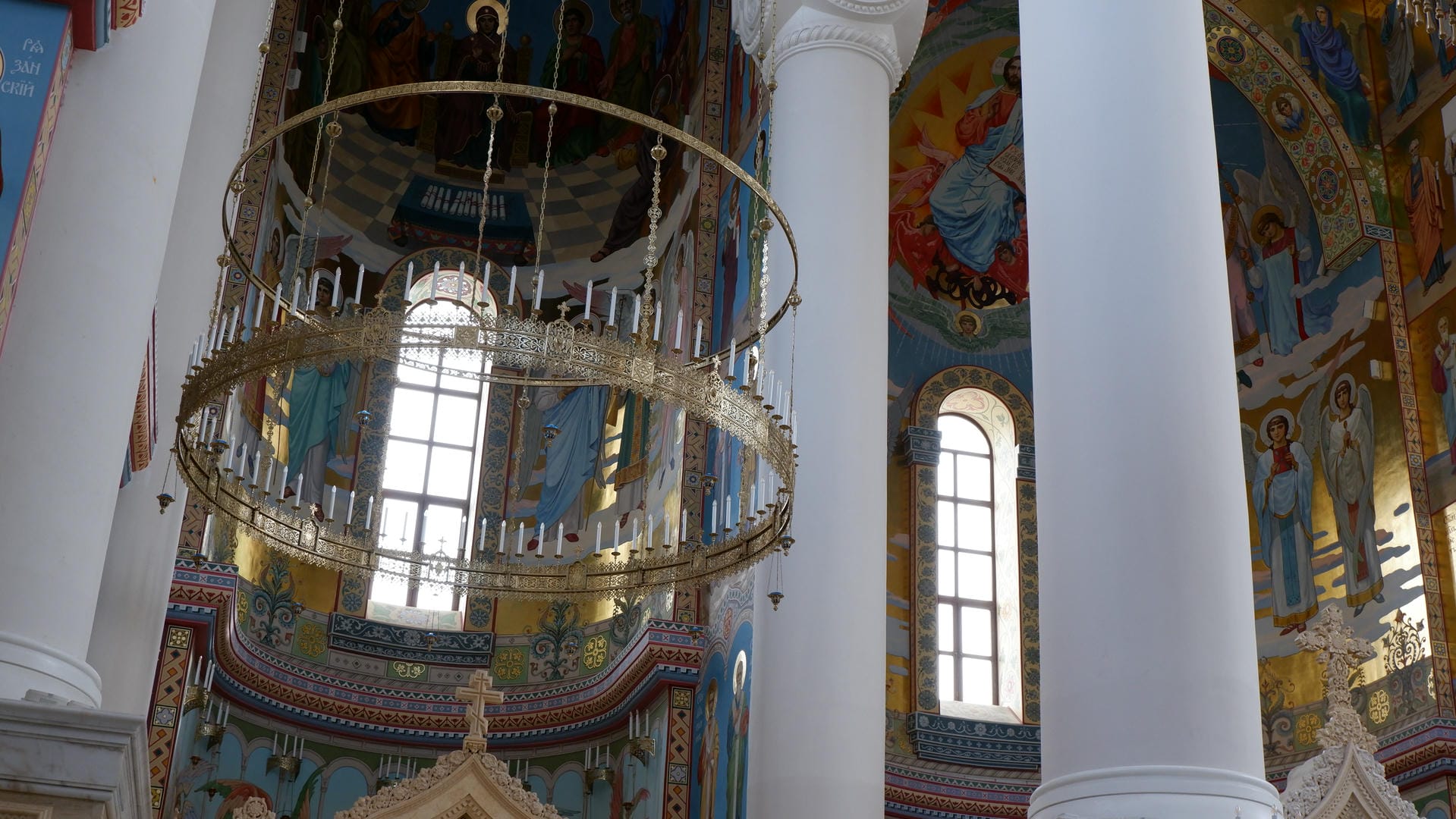 Inside the church, golden chandeliers hang from the ceiling, surrounded by colorful murals and white columns.